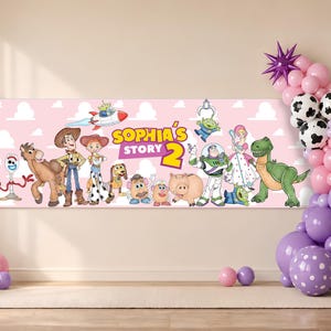May include: A rectangular horizontal banner with a light pink background featuring the text "SOPHIA'S STORY 2" and various animated toy characters including a cowboy, cowgirl, space ranger, dinosaur, pig, and aliens, accented by a balloon arch.