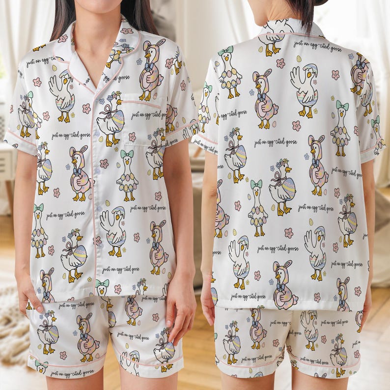 Puede incluir: Conjunto de pijama blanco con un estampado caprichoso de gansos. La camiseta de manga corta y los pantalones cortos presentan un patr&oacute;n repetido de gansos de dibujos animados con diferentes atuendos, con ribete rosa y el texto "just an egg-cited goose".