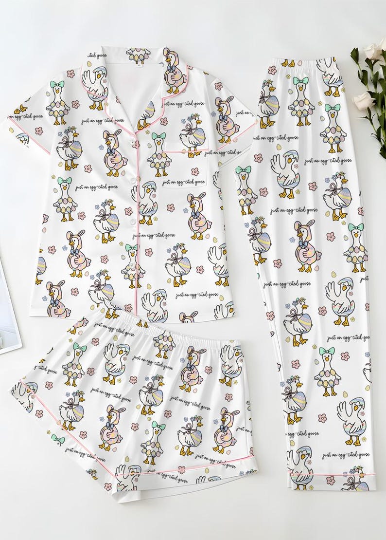 Puede incluir: Conjunto de pijama blanco con estampado de gansos. El conjunto incluye una camisa de manga corta con botones, pantalones cortos y pantalones largos. Cada pieza est&aacute; ribeteada con ribetes rosas y presenta un patr&oacute;n repetido de gansos de dibujos animados y flores. El texto "just an egg cited goose" tambi&eacute;n est&aacute; impreso.