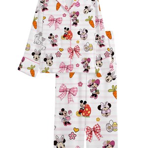 Puede incluir: Conjunto de pijama blanco con un estampado repetido de Minnie Mouse, zanahorias, huevos de Pascua y lazos. La parte superior de manga larga tiene una parte delantera abotonada y ribete rosa. Los pantalones tienen un estampado a juego con rayas rosas.