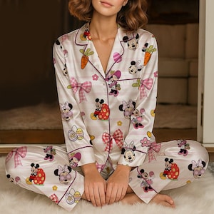 Puede incluir: Conjunto de pijama blanco con un estampado repetido de Minnie Mouse, huevos de Pascua, zanahorias y lazos rosas. La parte superior de manga larga y los pantalones est&aacute;n ribeteados con un borde morado. El conjunto de pijama est&aacute; hecho de un material suave y sedoso.