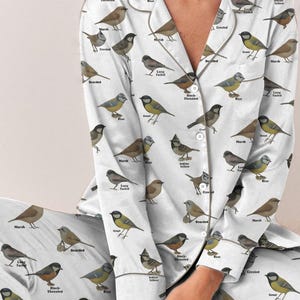 Puede incluir: Conjunto de pijama blanco con un patr&oacute;n repetido de ilustraciones de aves y sus nombres. La parte superior de manga larga y los pantalones tienen un dise&ntilde;o abotonado. Las aves son en tonos de marr&oacute;n, amarillo, azul y gris.