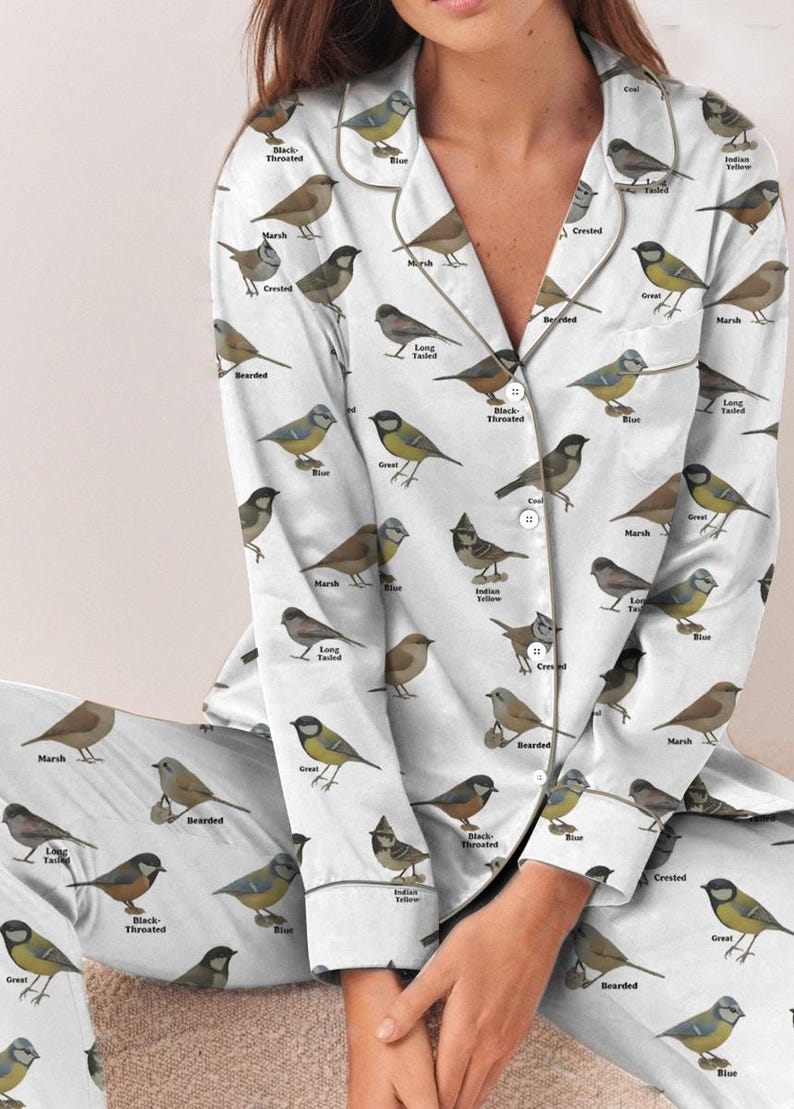 Puede incluir: Conjunto de pijama blanco con un patr&oacute;n repetido de ilustraciones de aves y sus nombres. La parte superior de manga larga y los pantalones tienen un dise&ntilde;o abotonado. Las aves son en tonos de marr&oacute;n, amarillo, azul y gris.