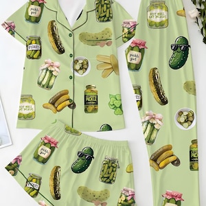 May include: Light green pajama set with a pickle theme. The set includes a short-sleeved button-up shirt, shorts, and long pants, all covered in pickle illustrations and text that reads "Pickle Girl" and "Hot Girls Eat Pickles."
