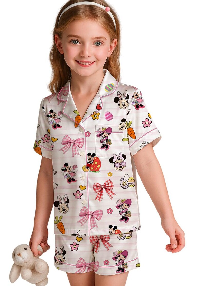 Puede incluir: Conjunto de pijama blanco con tem&aacute;tica de Pascua de Minnie Mouse. El conjunto incluye una camisa de manga corta con botones y pantalones cortos, ambos adornados con gr&aacute;ficos de Minnie Mouse, zanahorias, huevos y lazos rosas. El pijama tiene detalles de rayas rosas.