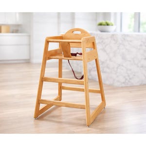 May include: A wooden high chair with a natural finish. The chair has a curved back, a seat, and a footrest. A red safety strap is visible. The high chair is designed for infants and toddlers.