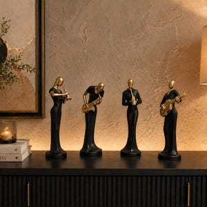 Peut inclure: Quatre figurines de musiciens noirs et dorés. Chaque figurine est dans une pose différente, jouant d'un instrument de musique. Les instruments comprennent une flûte, un saxophone, une trompette et une guitare. Les figurines sont exposées sur une surface noire.