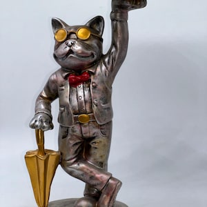 May include: A silver and gold decorative statue of a dog wearing a suit, bow tie, and glasses, holding a gold umbrella and a tray of wrapped candies. The statue has a vintage, distressed finish.