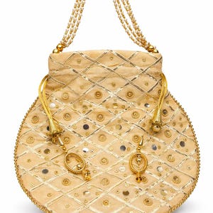 Könnte beinhalten: Eine beige, runde Handtasche mit Perlenhenkel und goldenen Akzenten. Die Tasche hat ein Rautenmuster mit goldenen Verzierungen, kleinen Spiegeln und dekorativen goldenen Anhängern. Der Griff besteht aus mehreren Strängen kleiner, weißer Perlen.