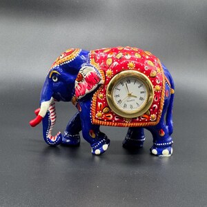 Könnte beinhalten: Dekorative Elefantenfigur in Blau, Rot und Gold mit Quarzuhr. Der Elefant hat detaillierte Muster und ein goldenes Zifferblatt mit schwarzen römischen Ziffern. Ein einzigartiges Dekorationsstück für das Zuhause.