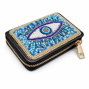 Könnte beinhalten: Schwarzes Portemonnaie mit einem Perlen-Design eines bösen Auges. Das Auge ist weiß, blau und rot, umgeben von blauen Perlen und einer goldenen Kettenborte. Es hat einen goldenen Reißverschluss und Zipper.