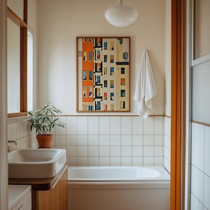 Könnte beinhalten: Ein Badezimmer mit weiß gefliesten Wänden, einer weißen Badewanne und einem Waschbecken auf einem Holzunterschrank. Ein gerahmter Druck eines orangefarbenen und beigen Wohnhauses hängt an der Wand. Ein weißes Handtuch hängt daneben, eine Pflanze steht im Topf.