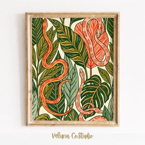 May include: A framed art print featuring a botanical pattern of various green leaves and three orange snakes winding through the foliage. The illustration uses a warm colour palette with deep forest green, olive, and bright orange tones on a cream background.