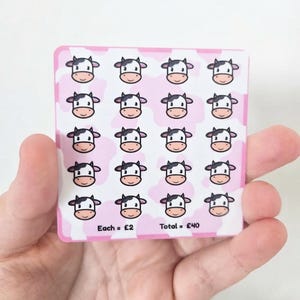 May include: A square sticker sheet featuring a repeating pattern of twenty cartoon cow faces against a light pink and white cow print background. The bottom of the sheet includes the printed text Each = £2 and Total = £40 in black font.
