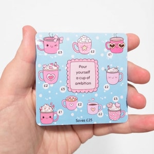 May include: A square light blue savings tracker card featuring various pink mug illustrations with different toppings and faces. The centre text reads Pour yourself a cup of ambition. Each mug is labelled with a pound symbol and a number, with the total text Saves £25 at the bottom.