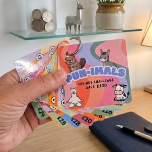 May include: A set of square savings challenge cards held on a metal ring, featuring colourful wavy backgrounds and cartoon animals. The top card displays the text PUN-IMALS SAVINGS CHALLENGE SAVE £200 with illustrations of a beaver, donkey, llama, and cow.