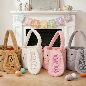 Peut inclure: Quatre paniers de Pâques en peluche marron, blanc, rose et gris, chacun avec des oreilles de lapin et un nom brodé sur une oreille. Les paniers sont sur un sol en bois avec des œufs de Pâques et des carottes. Une bannière "HAPPY" est suspendue.