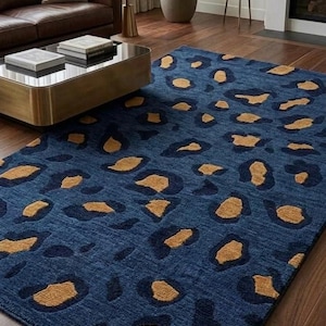 May include: A rectangular area rug featuring a deep blue base color with a repeating pattern of dark navy blue and golden tan leopard-style spots. The rug has a textured pile surface and is laid flat on a wooden floor in a living space.