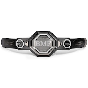 Può includere: Una cintura da campionato nera e argento con le lettere "BMF" al centro. La cintura ha un cinturino in pelle nera e dettagli argentati. Il testo "BMF 2019 EST." è su un lato e "ANYONE ANYTIME ANYWHERE" sull'altro.