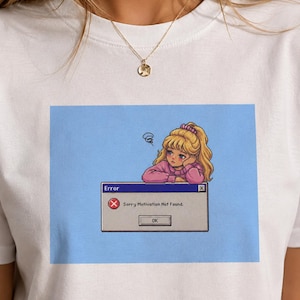 Könnte beinhalten: Weißes T-Shirt mit einer Grafik eines traurigen Anime-Mädchens mit blonden Haaren. Die Grafik ist ein blaues Quadrat mit einer Fehlermeldung "Sorry Motivation Not Found."
