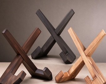 May include: Three X-shaped wooden stands for displaying items, each featuring a distinct wood grain finish. One stand is dark brown, one is charcoal black, and one is a light natural tan color, all with angled supports.