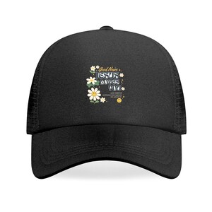 Könnte beinhalten: Schwarze Trucker-Cap mit gebogenem Schirm und Mesh-Rücken. Auf der Vorderseite befindet sich ein Blumendesign mit dem Text "Good News, Jesus Loves You" in einer verspielten Schriftart. Das Design umfasst Gänseblümchen und ein lächelndes Gesicht.