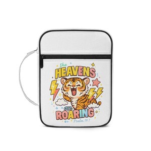 May include: White crossbody bag with a black zip and strap. The bag displays a colourful graphic of a cartoon tiger with the text "the HEAVENS are ROARING" and "Psalm 19:1". The tiger is orange and brown with yellow lightning bolts.