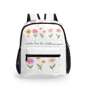 Puede incluir: Mochila blanca con un diseño floral de flores rosas y amarillas y el texto "consider how the wildflowers grow". Tiene bolsillos laterales de malla negra y correas negras.