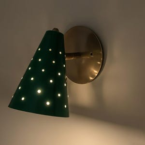 Puede incluir: Aplique de pared verde en forma de cono con una placa de montaje y un brazo de color lat&oacute;n. La l&aacute;mpara tiene una serie de peque&ntilde;os puntos blancos espaciados uniformemente. El aplique est&aacute; dise&ntilde;ado para montarse en la pared.