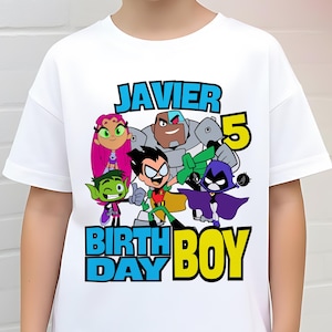 May include: White t-shirt featuring a colorful graphic of the Teen Titans Go! characters, the name "JAVIER", the number "5", and the words "BIRTH DAY BOY". The shirt is worn by a young boy.