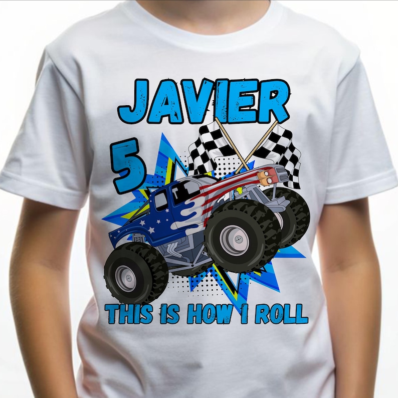 A white t-shirt for a 5-year-old boy featuring a large monster truck decorated with a blue and red American flag pattern. The name "JAVIER" is printed in bold blue letters at the top, a large blue number "5" is on the left, and the text "THIS IS HOW I ROLL" is at the bottom. Two checkered racing flags are crossed behind the truck.