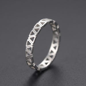 May include: A silver-toned ring featuring a continuous band design composed of repeating open triangular cutouts. The metal surface has a smooth, polished finish, and the geometric pattern extends around the entire circumference of the circular band.