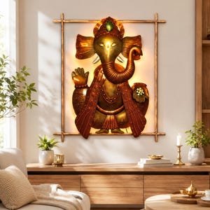 Può includere: Un'opera d'arte da parete in metallo color oro che raffigura la divinità Ganesha, incorniciata da un sottile bordo in metallo color bronzo. La figura presenta una proboscide, grandi orecchie e una corona, illuminata da una luce calda.