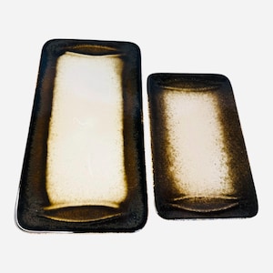 May include: A set of three ceramic mugs with a speckled, matte finish. The mugs are in shades of cream, light gray, and dark gray. Each mug has a simple, modern design and a rounded handle. The mugs are stacked on top of each other.