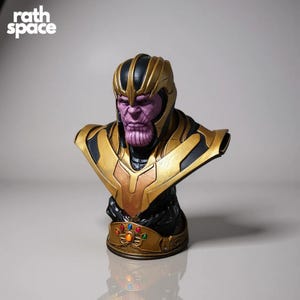 May include: A Thanos bust figurine with a purple face, gold helmet, and armor. The bust features the text "rath space" in the upper left corner. The Infinity Gauntlet is visible on the base of the bust.