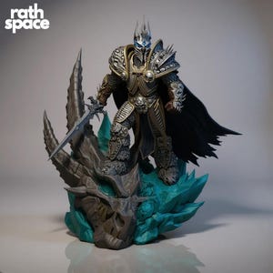 以下が含まれることがあります： 銀と金の鎧を着た戦士の精巧なフィギュア。剣を持ち、ドラゴンの頭蓋骨とターコイズのクリスタルベースの上に立っています。黒いマントと王冠を身に着けています。「rath space」の文字が左上にあります。