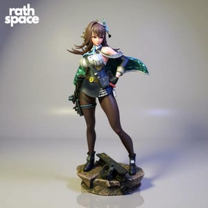 Puede incluir: Figura detallada de un personaje femenino con un atuendo de inspiración militar. La figura tiene cabello castaño y viste un top blanco y negro, una capa verde y botas negras. La base de la figura es una estructura rocosa. El texto "rath space" está en la esquina superior izquierda.