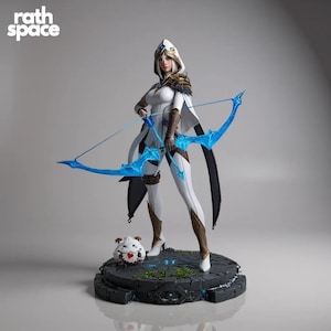 Puede incluir: Figura detallada de una arquera con un atuendo blanco y dorado, sosteniendo un arco azul. La figura está sobre una base de piedra con una pequeña criatura blanca con un corazón en el pecho. El logo de Rath Space está en la esquina superior izquierda.