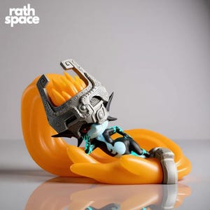 May include: A figurine of a character with a silver helmet and black and blue bodysuit, resting on a large orange hand. The character has a pale blue face and red eyes. The figurine is set against a light grey background. The text "rath space" is in the upper left corner.