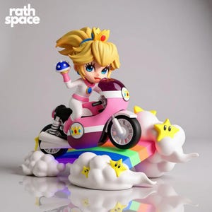 Peut inclure: Figurine de la Princesse Peach sur un scooter rose et violet, sur une base arc-en-ciel et nuage. La figurine tient un objet bleu pointu. La base a des étoiles jaunes. Le texte "rath space" est dans le coin supérieur gauche.
