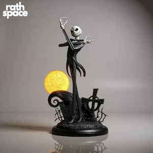 Può includere: Una statuetta in bianco e nero di Jack Skellington da The Nightmare Before Christmas, con una luna gialla e una base di cimitero. La statuetta è in piedi con le braccia tese. Il testo "rath space" è in alto a sinistra.