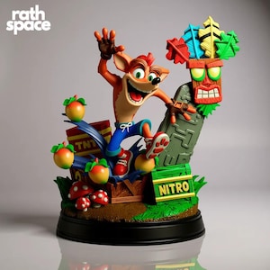 Puede incluir: Una vibrante estatua de Crash Bandicoot en una pose dinámica, saltando sobre una caja de TNT y rodeado de elementos coloridos. La estatua presenta una máscara Tiki detallada, manzanas y la palabra "NITRO". La base es negra, y la estatua tiene el texto "rath space".
