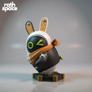 Puede incluir: Figura estilizada de un conejo, con cuerpo negro, cabeza blanca y detalles en naranja. La figura tiene una bufanda, un botón verde y una base con detalles dorados. El texto "rath space" está en la esquina superior izquierda.