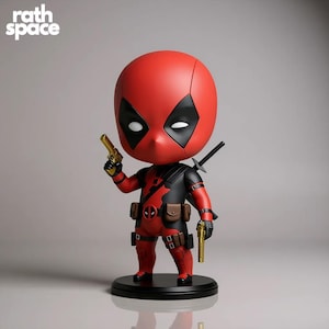 Può includere: Statuetta di Deadpool rossa e nera con una testa grande, occhi neri e una maschera nera. La statuetta tiene in mano due pistole d'oro e una spada è attaccata alla schiena. La base è nera e il testo "rath space" è in alto a sinistra.
