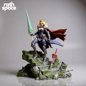 Op de afbeelding: Gedetailleerd beeldje van een vrouwelijke krijger in een blauw en zilveren outfit, met een groene speer en een rode cape. Het beeldje staat op een stenen trap met een zwaard en de tekst "rath space".