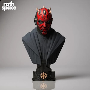 Puede incluir: Busto de Darth Maul, con rostro rojo y negro, cuernos y túnica gris oscura. El busto está montado sobre una base negra con un emblema dorado. El texto "rath space" está en la esquina superior izquierda.