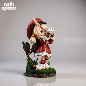 Puede incluir: Una figura de un personaje con un atuendo rojo y blanco, sosteniendo un objeto blanco. La figura tiene cabello rubio y está de pie sobre un trozo de hierba verde con pequeñas criaturas blancas y negras. El texto "rath space" está en la esquina superior izquierda.