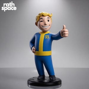 May include: A Vault Boy figurine with blonde hair, winking and giving a thumbs up. The character wears a blue jumpsuit with a yellow trim and the number 33 on the chest. The figure stands on a black circular base with the text rath space visible.