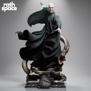 Può includere: Una statua da collezione dettagliata di una figura calva con una lunga veste fluida verde scuro, che tiene in alto una fiala verde brillante. Un grande serpente avvolto con la bocca aperta si trova sulla base rocciosa. Il testo recita rath space.