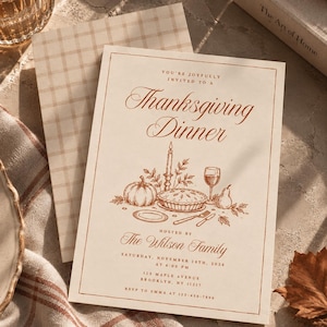 May include: A cream-colored Thanksgiving dinner invitation card with copper-toned text and illustrations. The design features a pumpkin, a pie, a candle, a wine glass, and a pear. It includes the text: You're joyfully invited to a Thanksgiving Dinner, hosted by The Wilson Family, Saturday, November 28th, 2026 at 6:00 PM, 123 Maple Avenue, Brooklyn, NY 11217, RSVP to Emma at 123-456-7890.